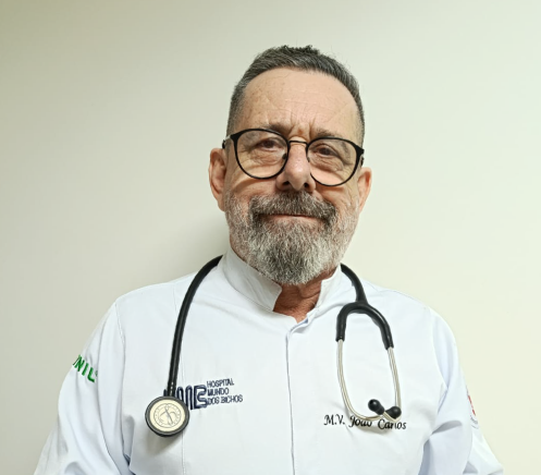 Mulher vestindo uniforme cirúrgico verde-azulado e estetoscópio, braços cruzados, sorrindo.