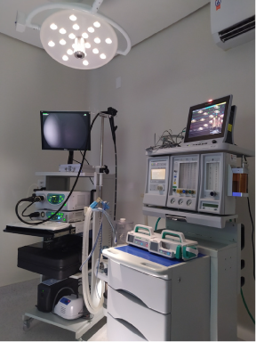 Sala de cirurgia equipada com monitores, luzes e máquina de anestesia.
