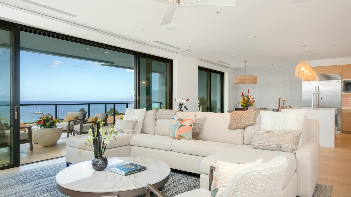 Bright, airy living room with ocean view, large sectional sofa, round coffee table, and open kitchen.