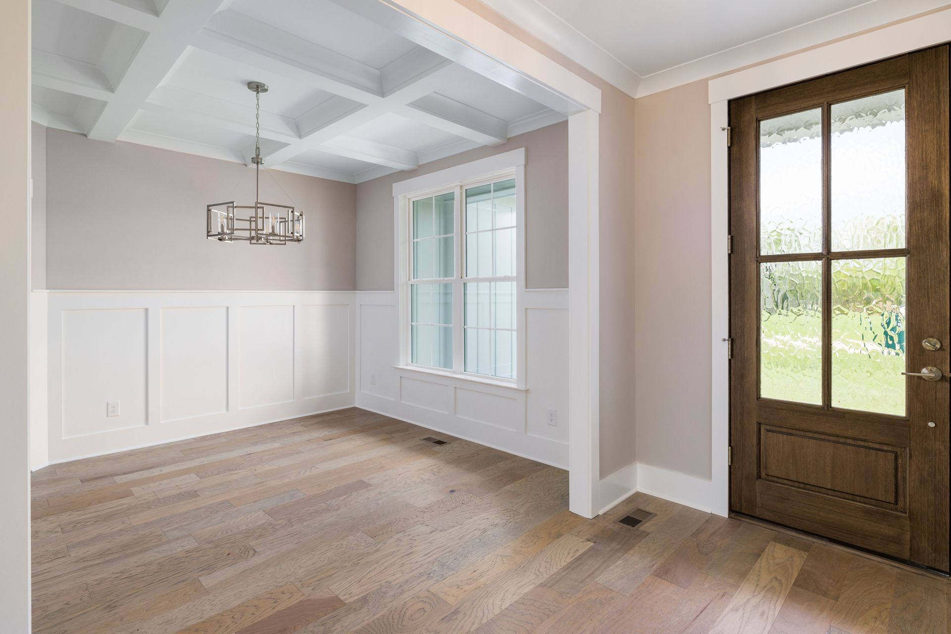 Bright empty dining room with white paneling, hardwood floors, and a glass-paneled wooden door