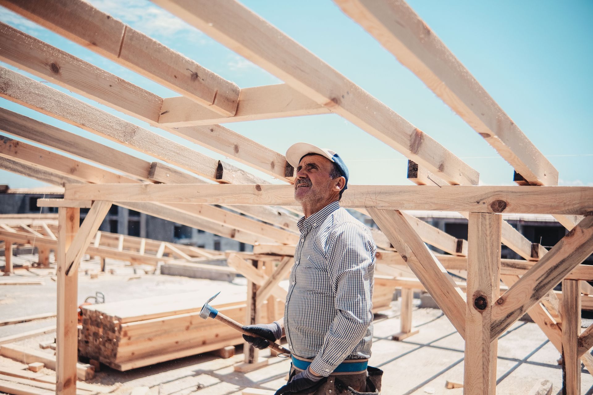 Worker inspecting wooden roof framing at a construction site under a clear sky