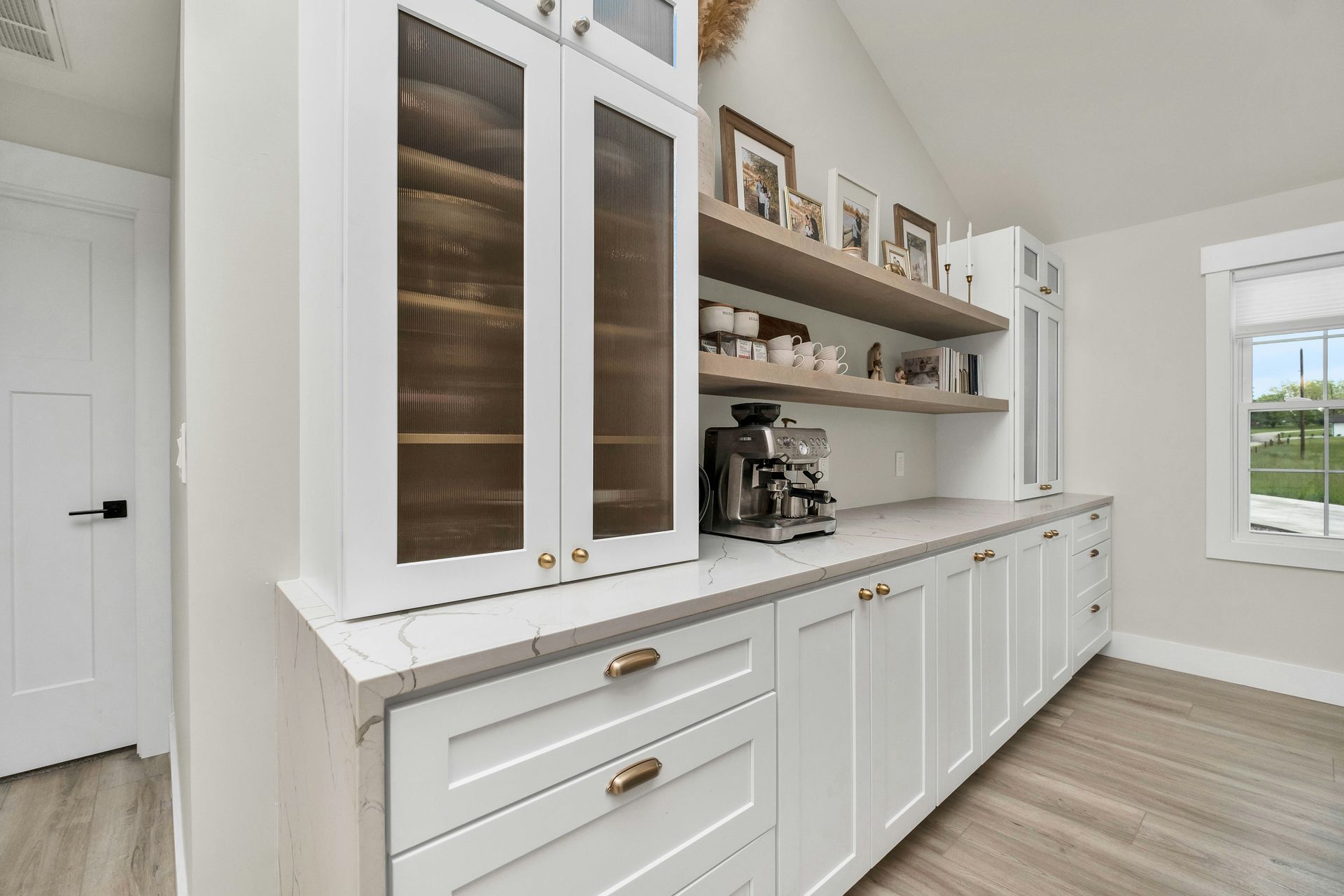 Bright white kitchen pantry with glass cabinets, open shelves, coffee maker, and built-in storage along the wall