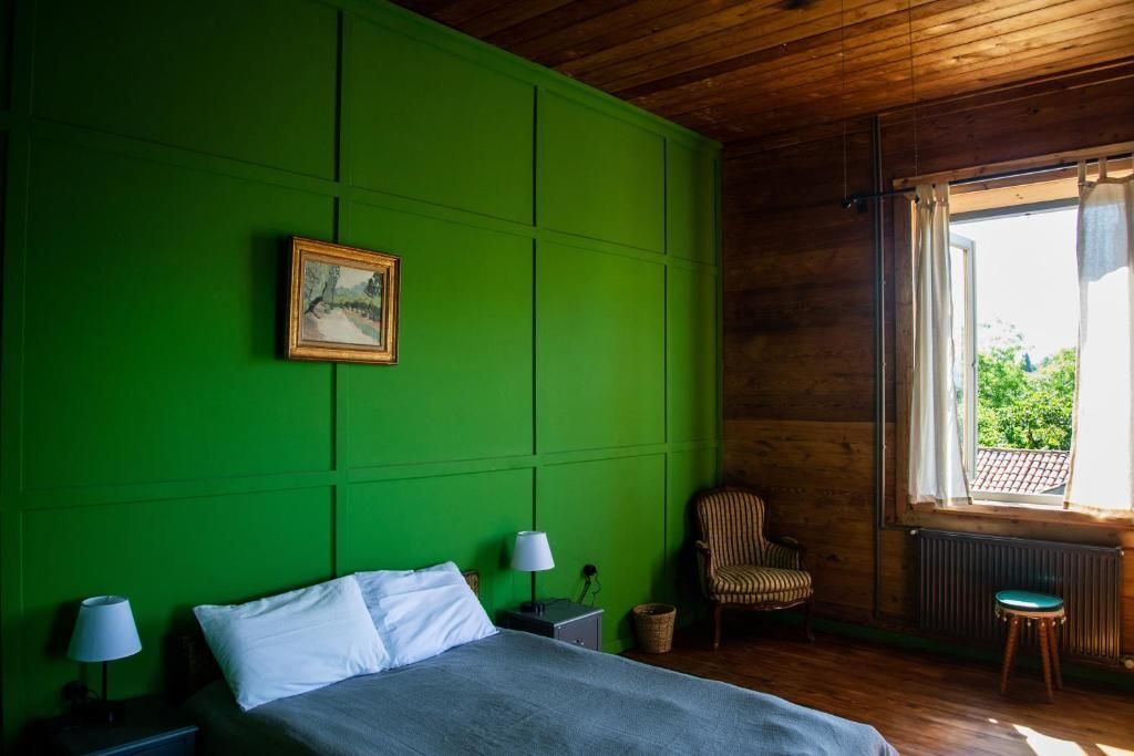 A bedroom with green walls , a bed , a chair and a window.