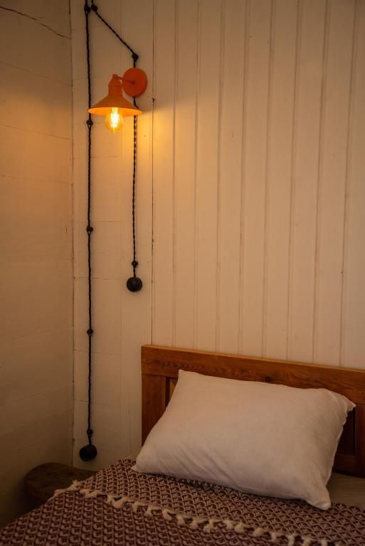 A bed with a pillow and a lamp on the wall above it.