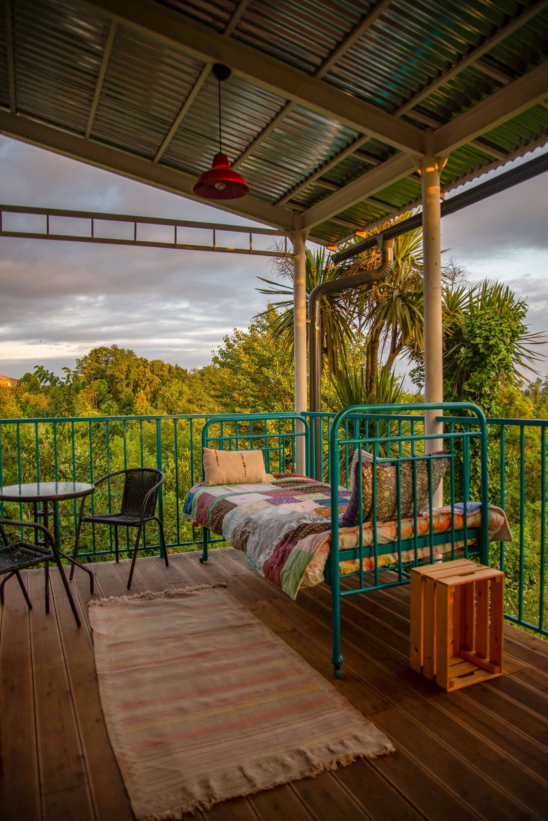 There is a bed on the balcony with a view of the trees.