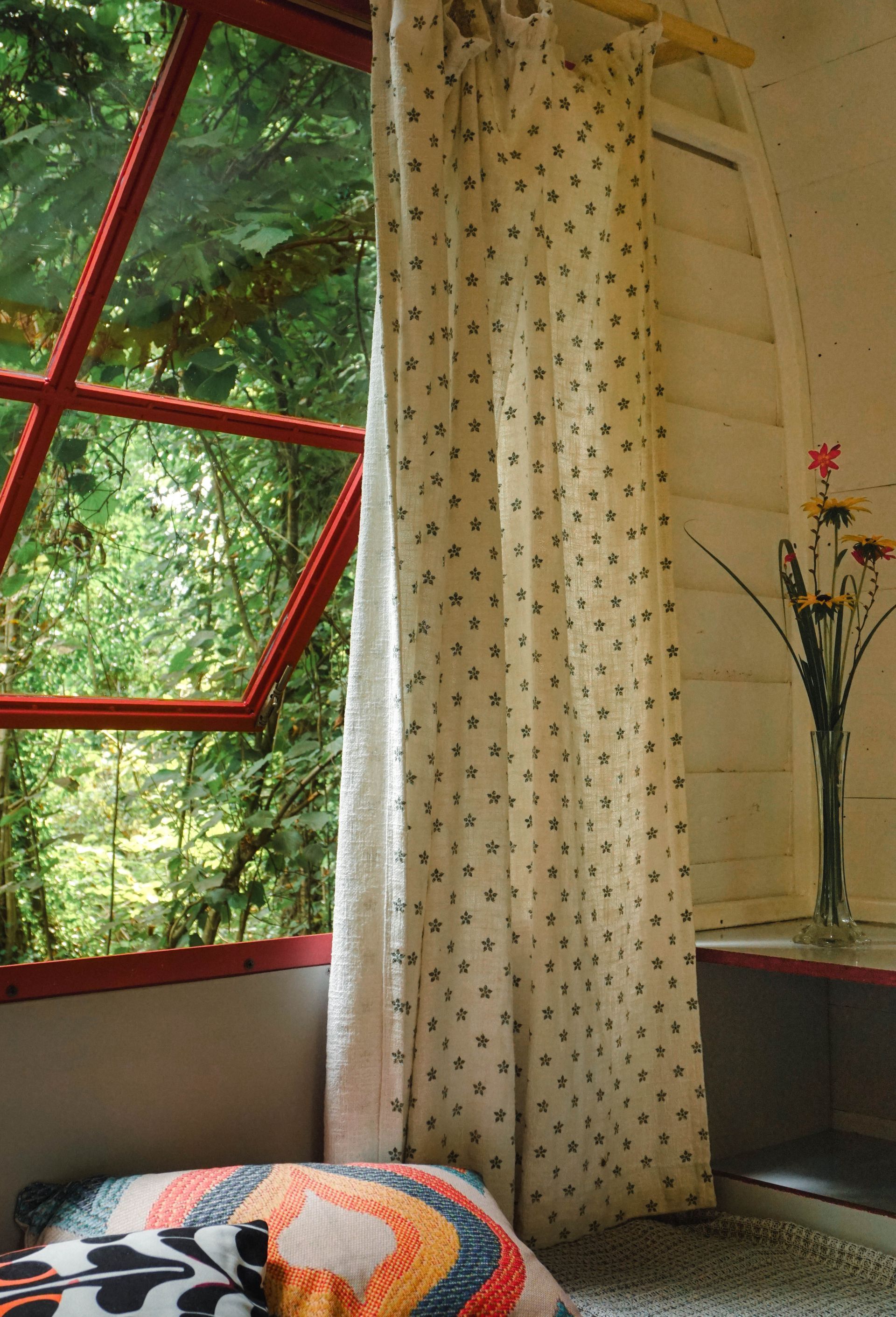 A room with a pillow and a vase of flowers in front of a window.