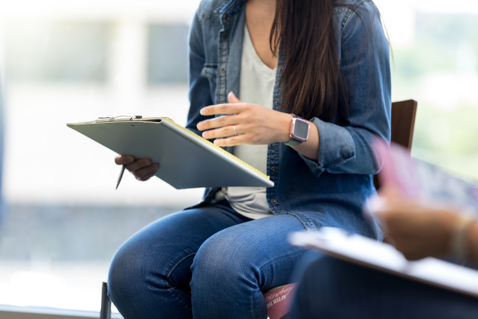 A woman is sitting in a chair holding a clipboard.