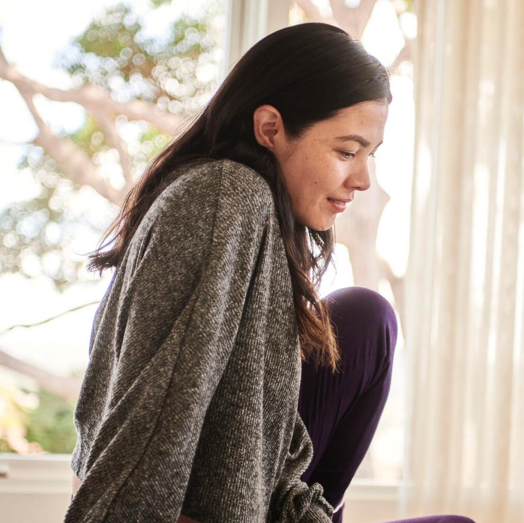 A woman in a grey sweater is squatting down in front of a window
