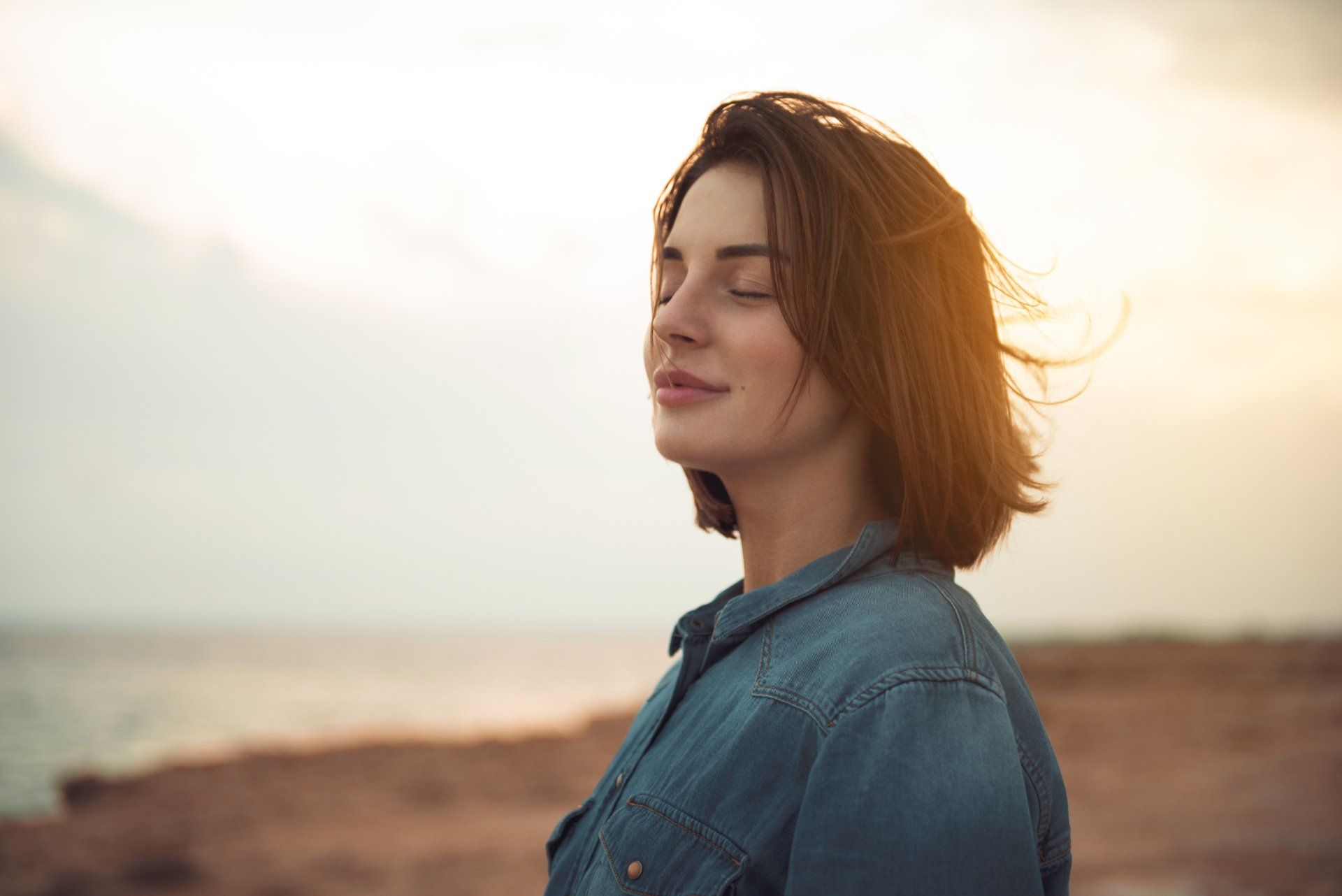 A woman is standing on a beach with her eyes closed.