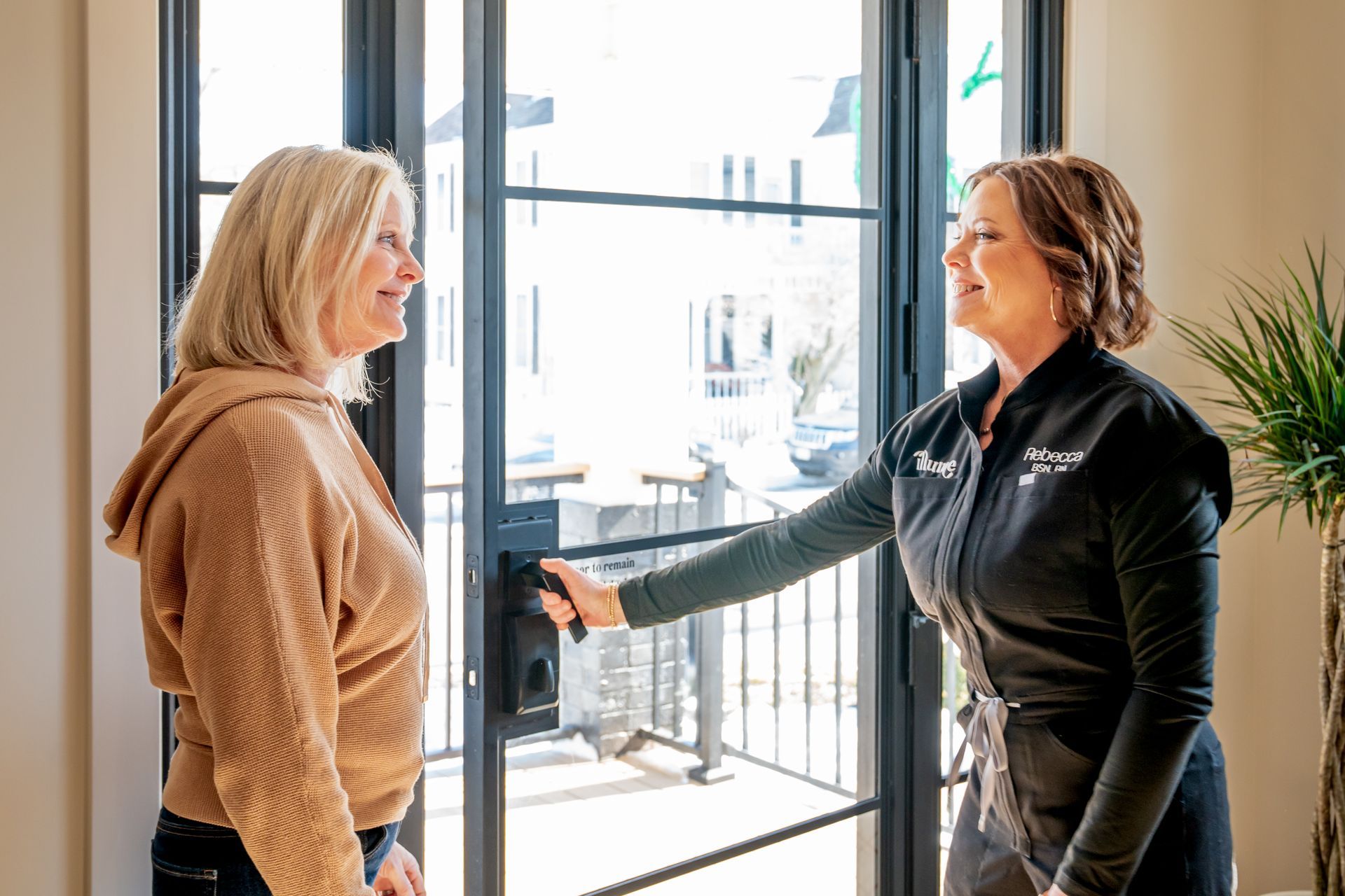 Two women are standing next to each other in front of a window.