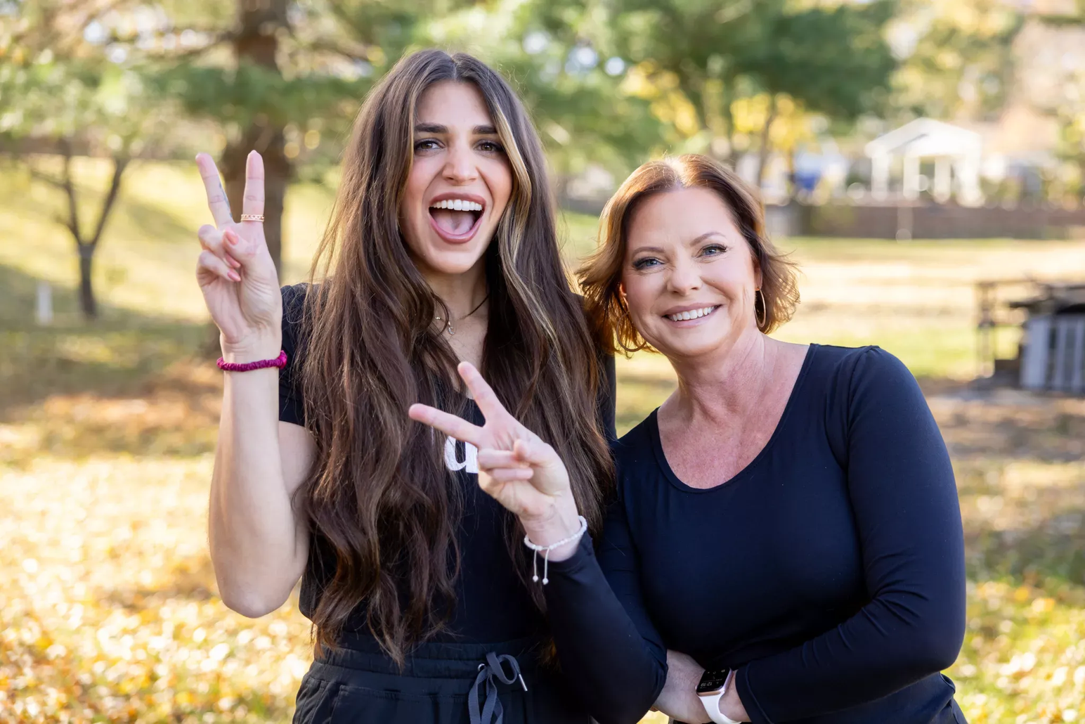 Two women are standing next to each other and making peace signs.