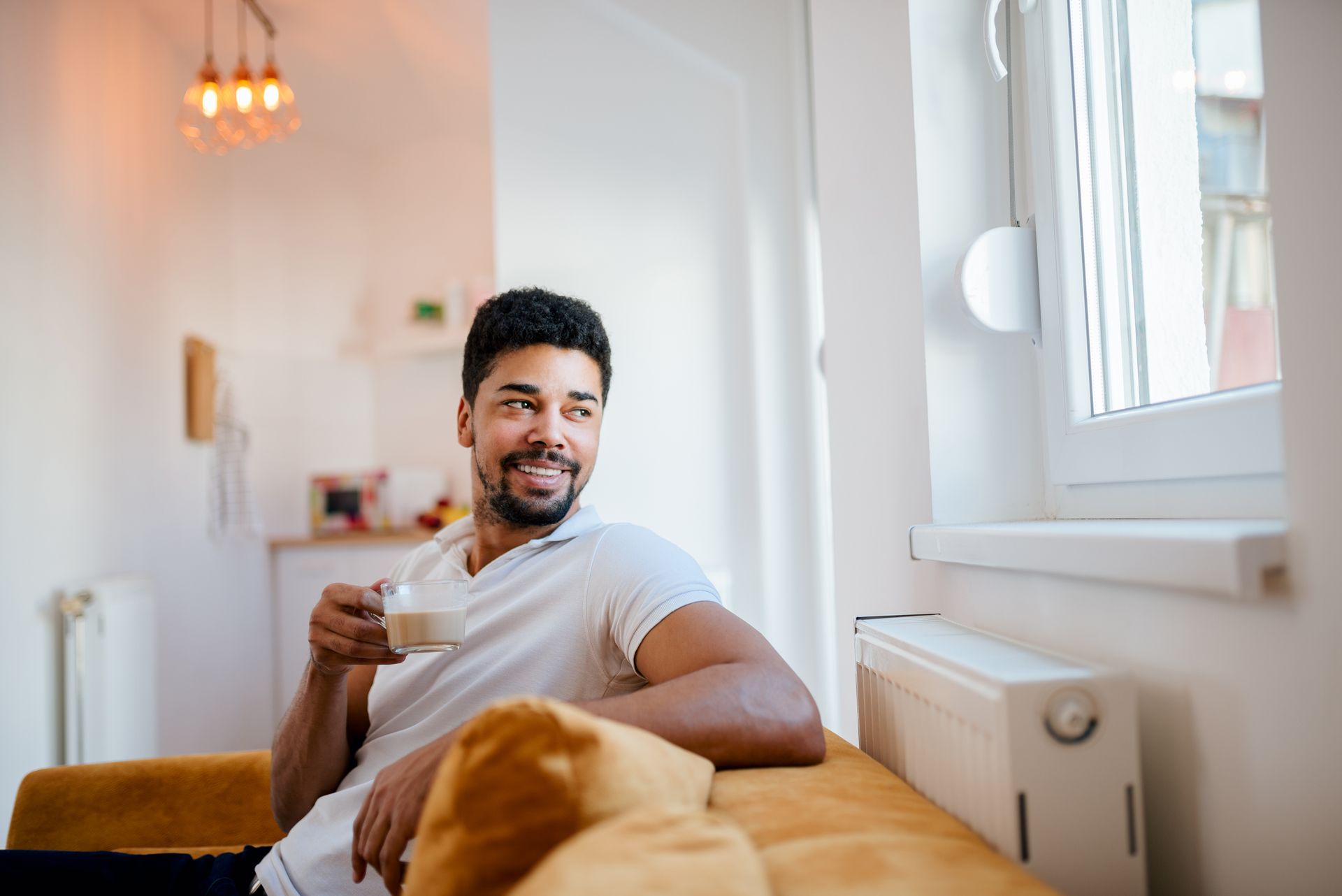 A man is sitting on a couch holding a cup of coffee and looking out the window.