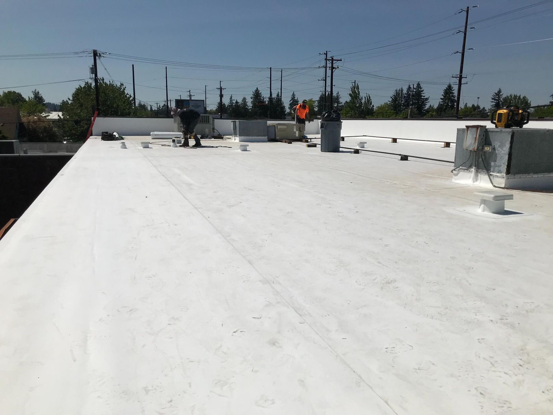 Workers on a flat white commercial roof, installing equipment on a sunny day.