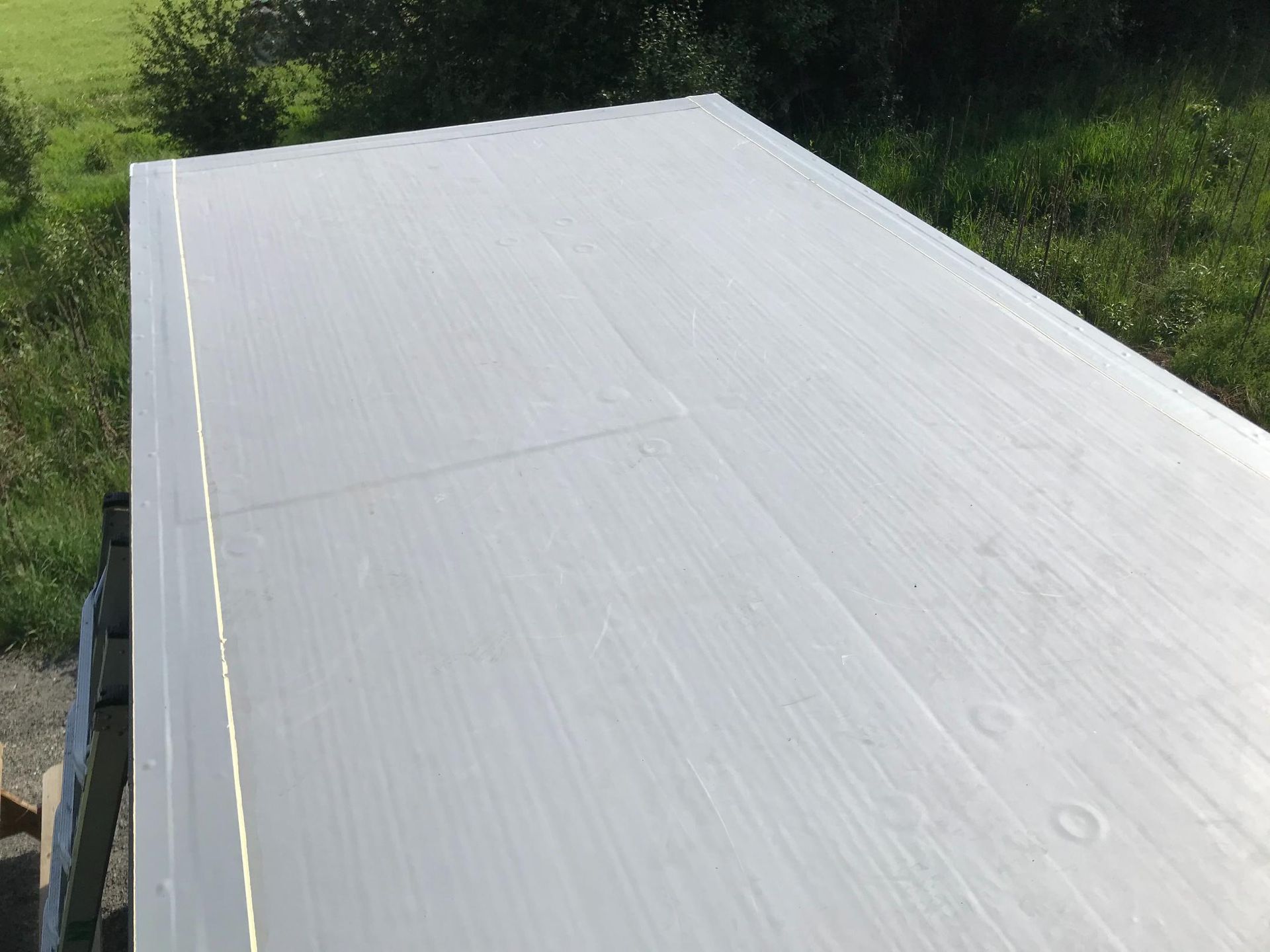 A flat, white roof with a slight slope, next to green grass and foliage.