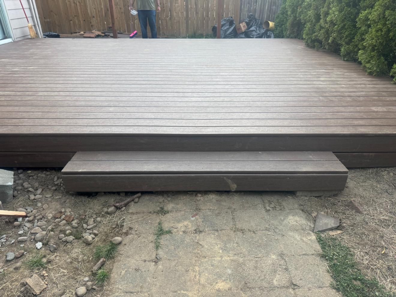 Brown composite deck with step, leads to a backyard with a person standing.