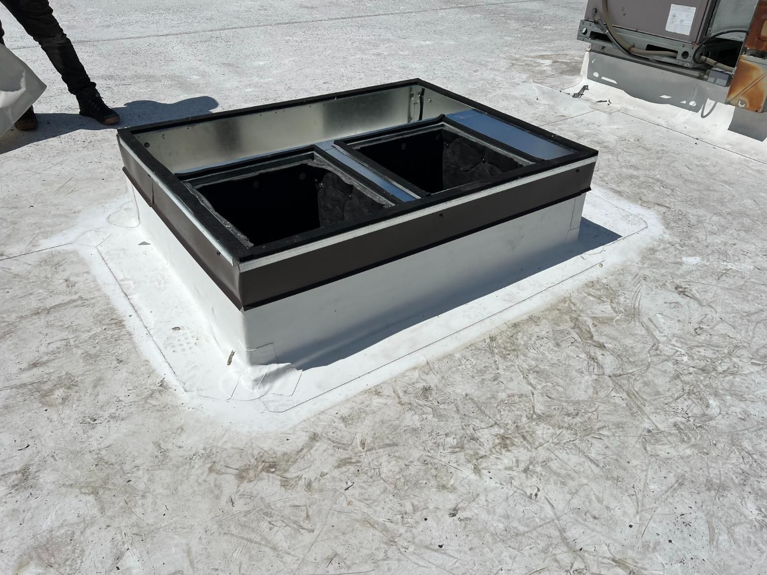 Skylight on a white rooftop. Dark box interior, white border, brown trim, person's leg visible.