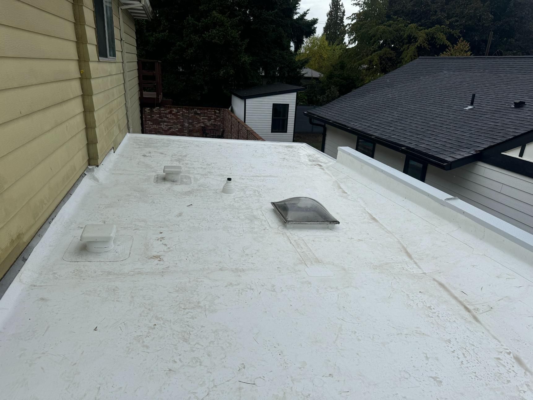 White flat roof with vents and a skylight; adjacent to a yellow building and a black-roofed structure.