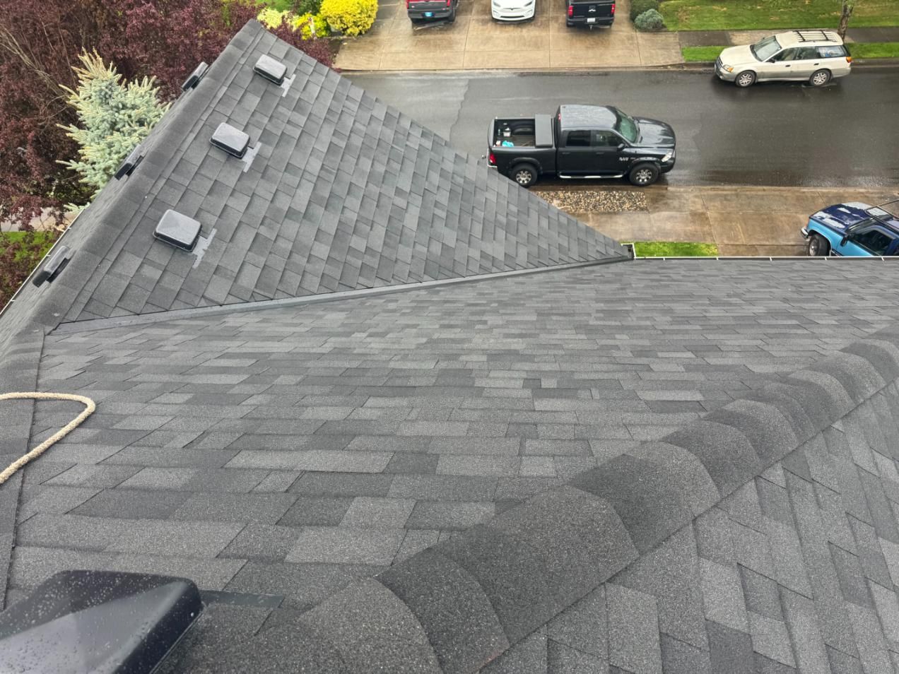 Asphalt shingle roof with vents, overlooking a street with parked cars and a black pickup truck.