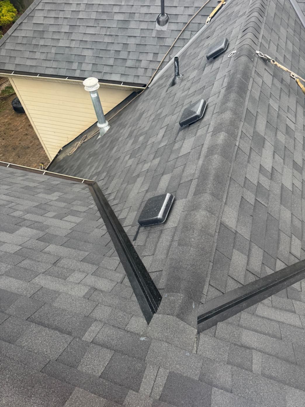 Dark gray shingle roof with vents. Black flashing and a chimney pipe.