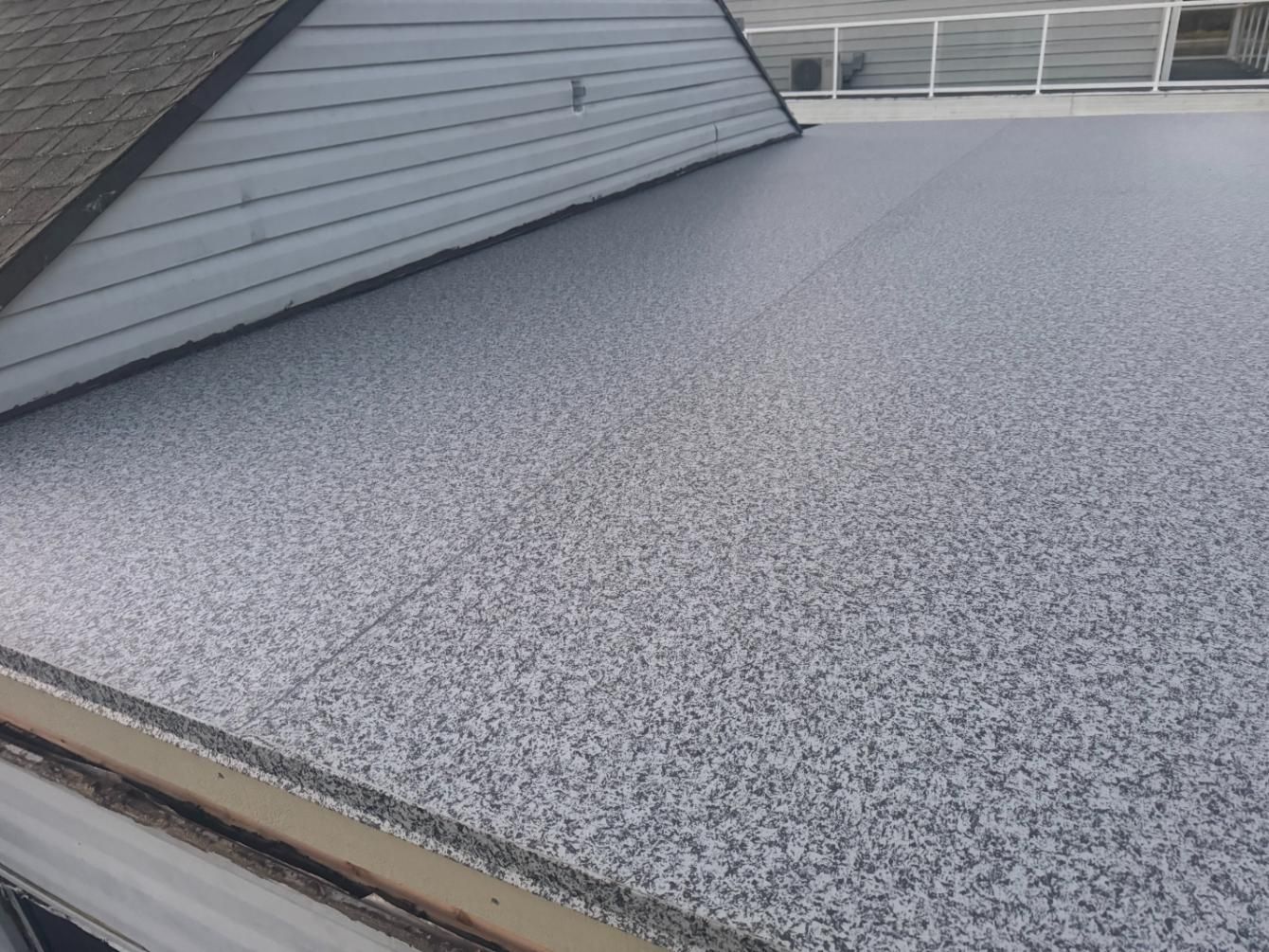 Flat roof with gray and white speckled coating, next to a slanted shingled roof.