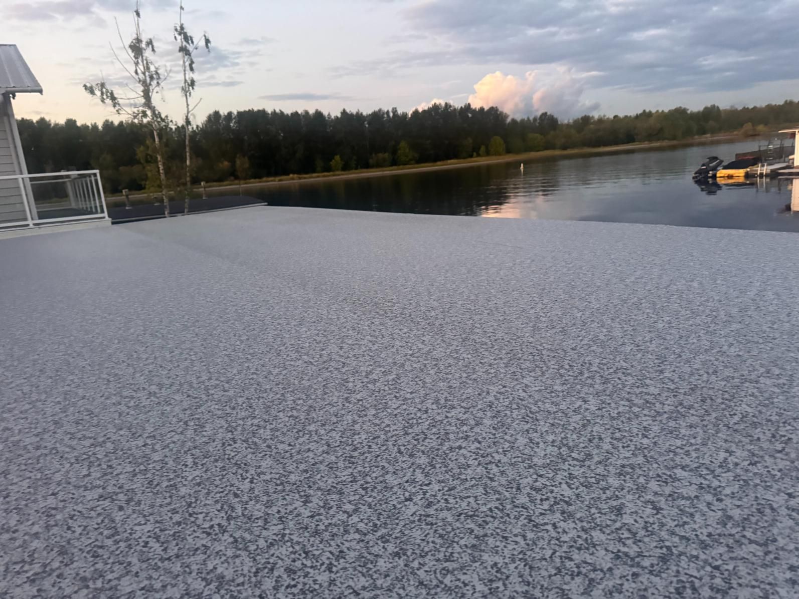 Granular, light-colored surface overlooking calm water and treeline at dusk.