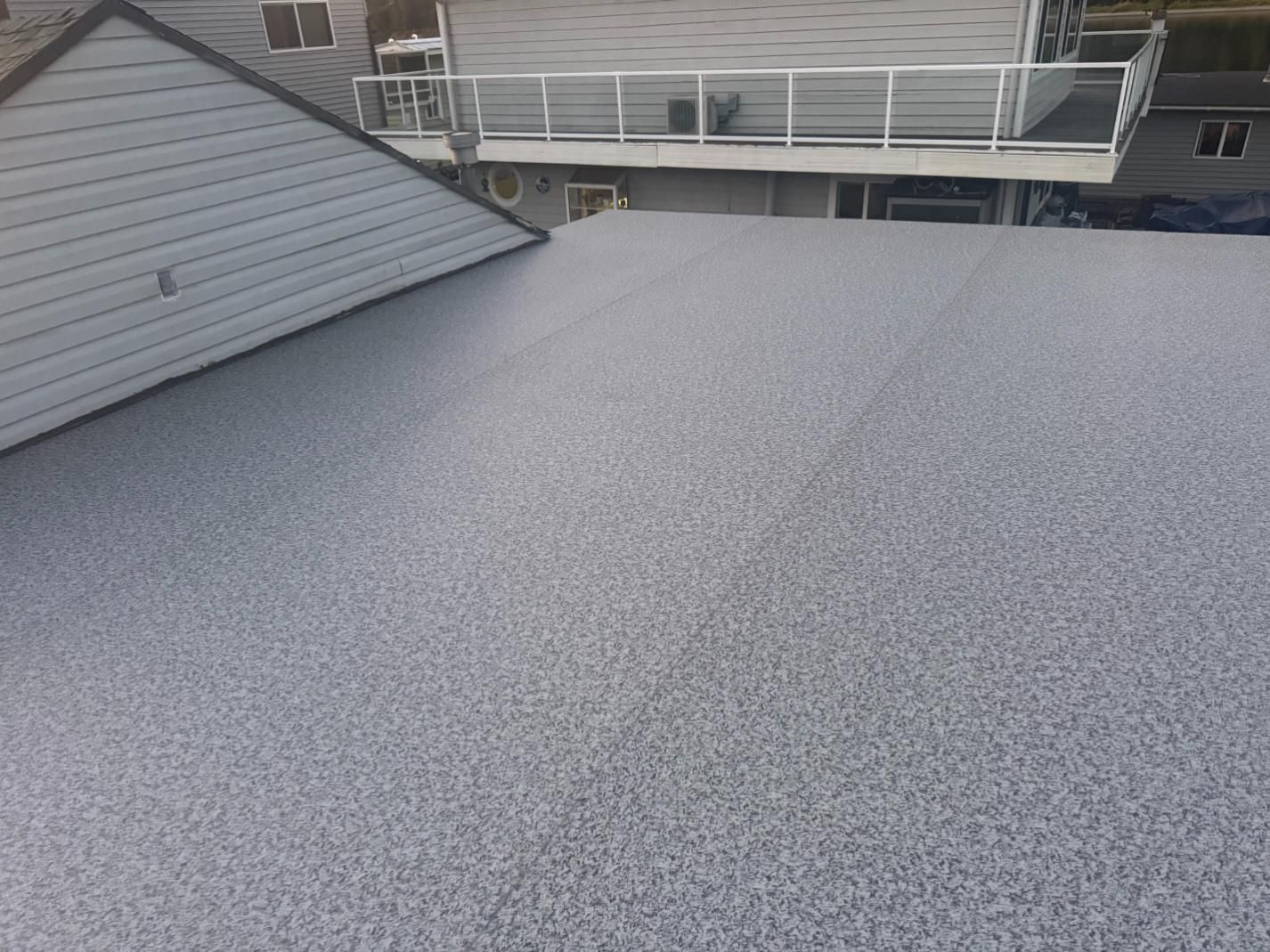 Gray pebble-textured roof of a house, with another house and deck visible in the background.