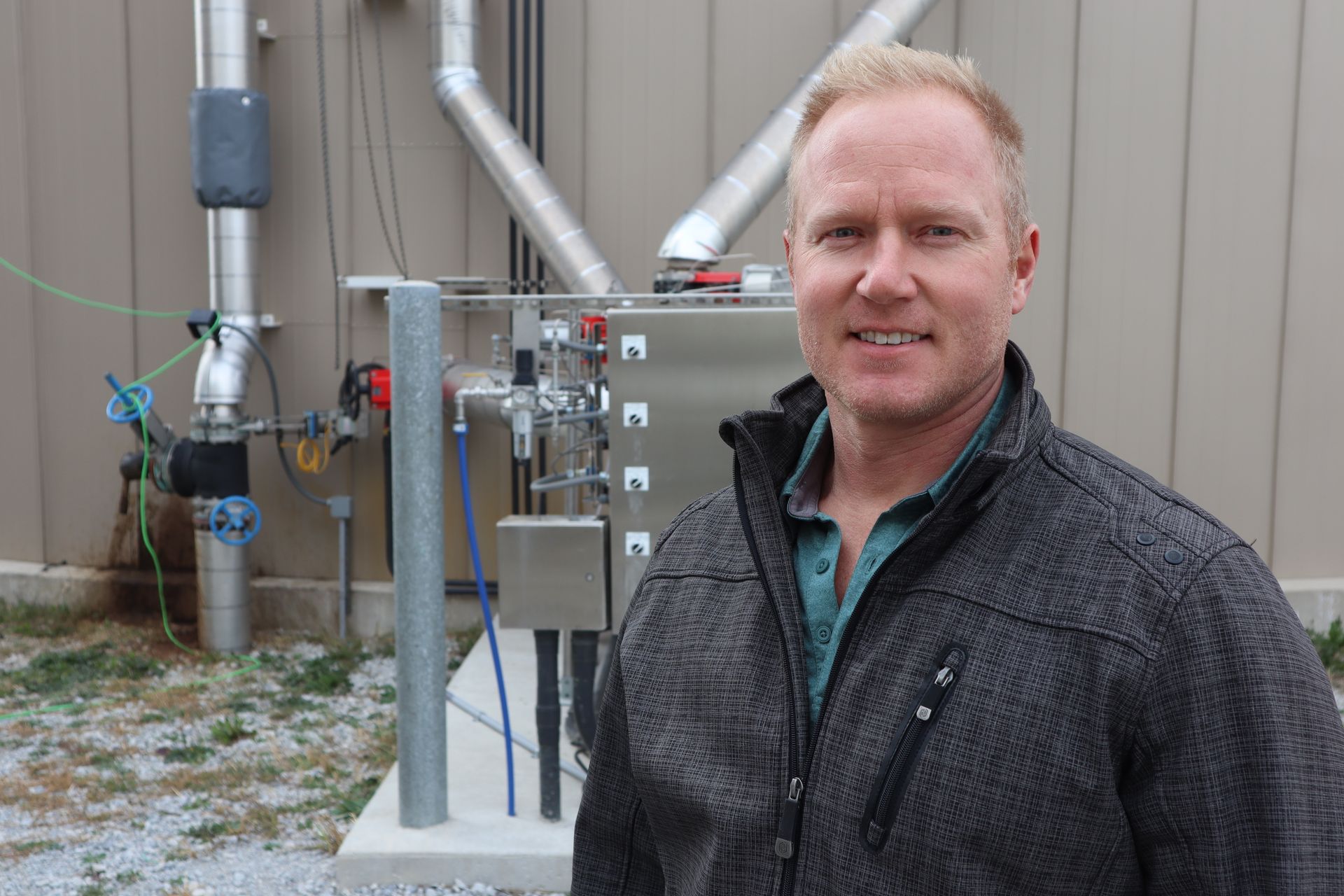 A man in a gray jacket is standing in front of a building.