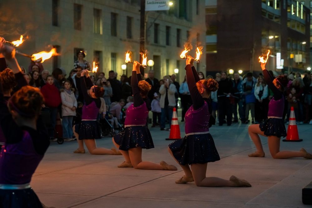 A group of cheerleaders are kneeling down and holding flames in front of a crowd.