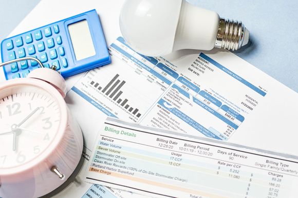 An alarm clock , calculator , light bulb and bills on a table.