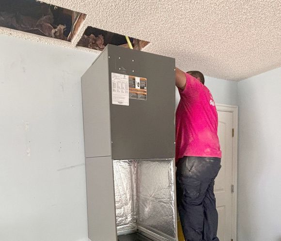 A man is standing on a ladder fixing an air conditioner.