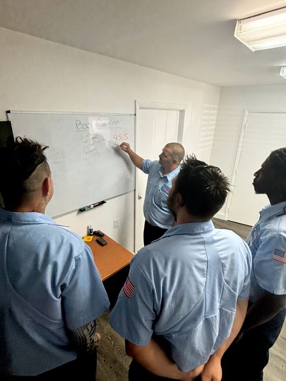 A group of men in blue shirts are standing around a whiteboard.