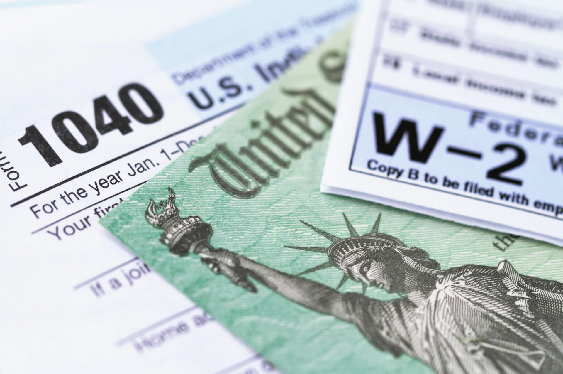 Tax forms 1040 and W-2 alongside a green $20 bill with the Statue of Liberty.