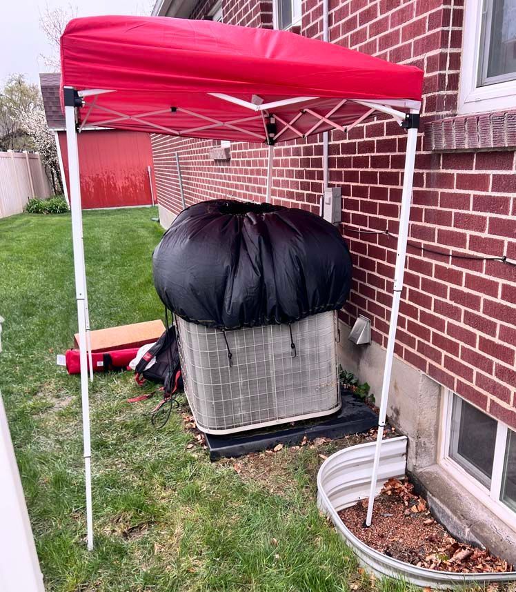 A red canopy is covering an air conditioner outside of a brick house.