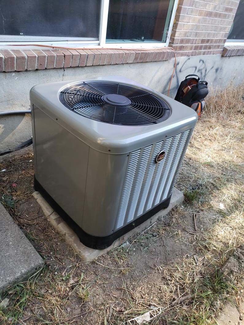 An air conditioner is sitting outside of a brick house.