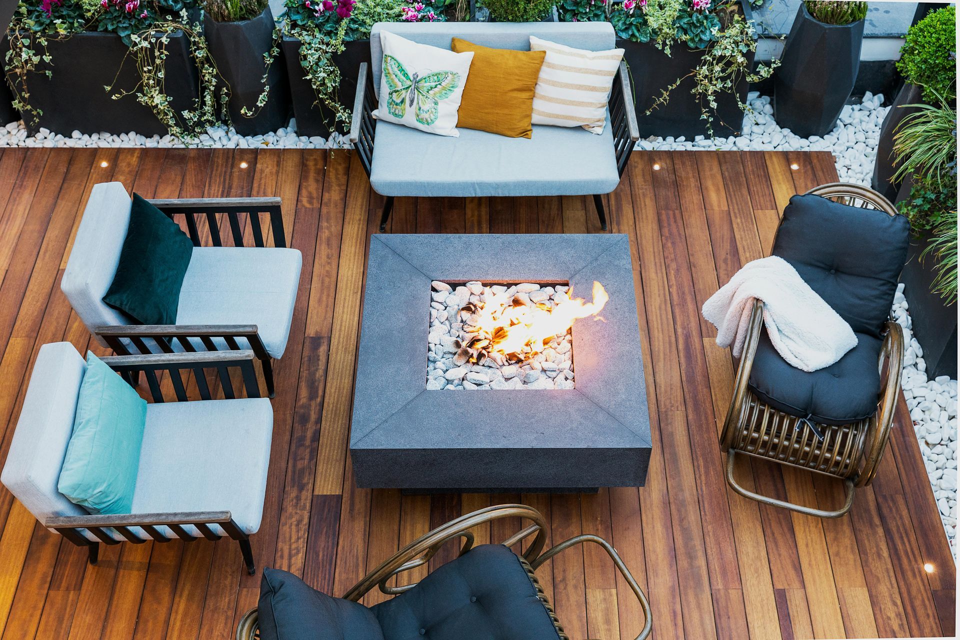 A wooden deck with a fire pit surrounded by chairs and a couch.