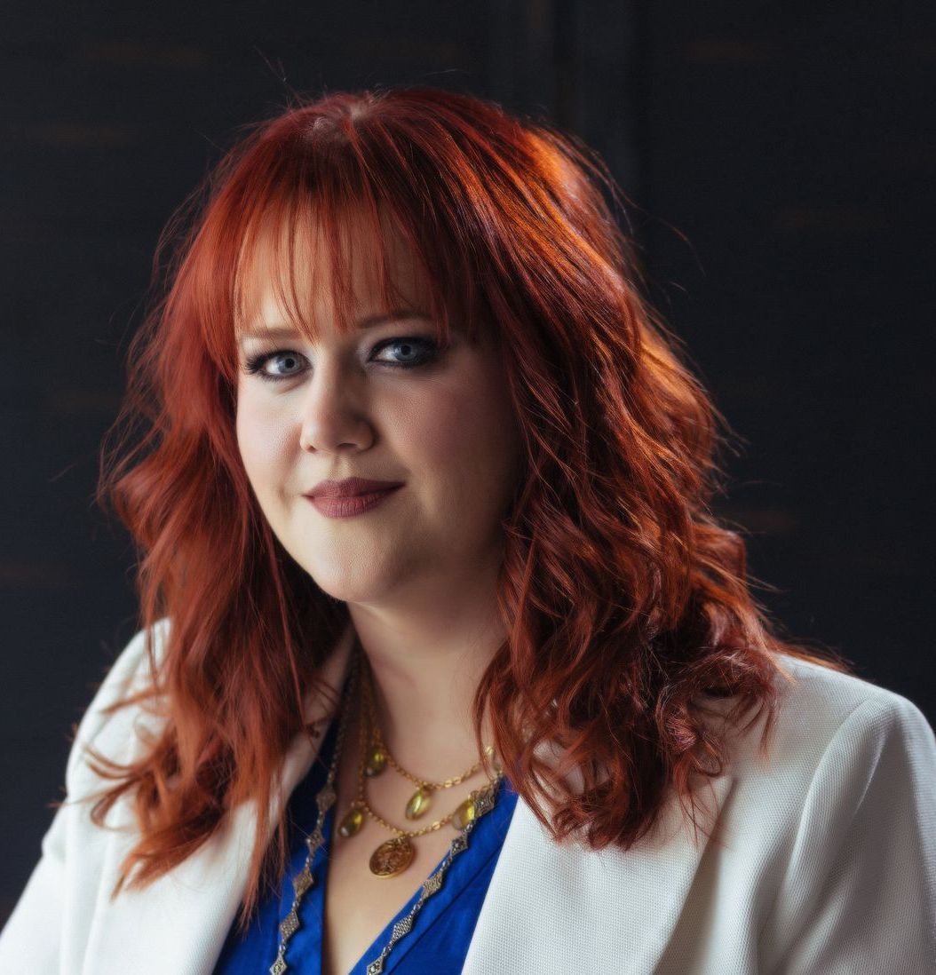 A woman with red hair is wearing a white jacket and a blue shirt