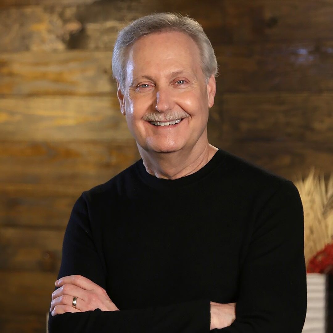 A man in a black sweater is smiling with his arms crossed