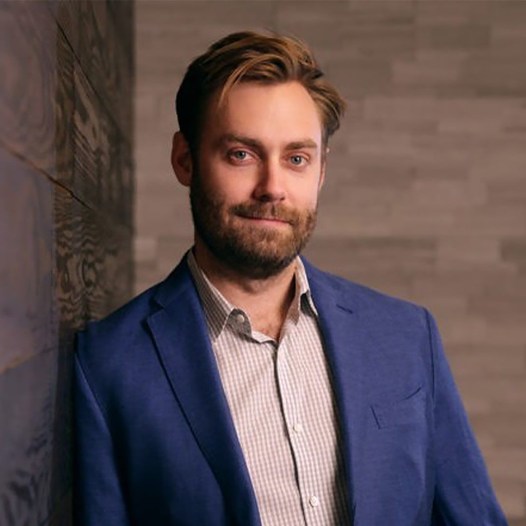 A man in a blue suit is leaning against a brick wall.