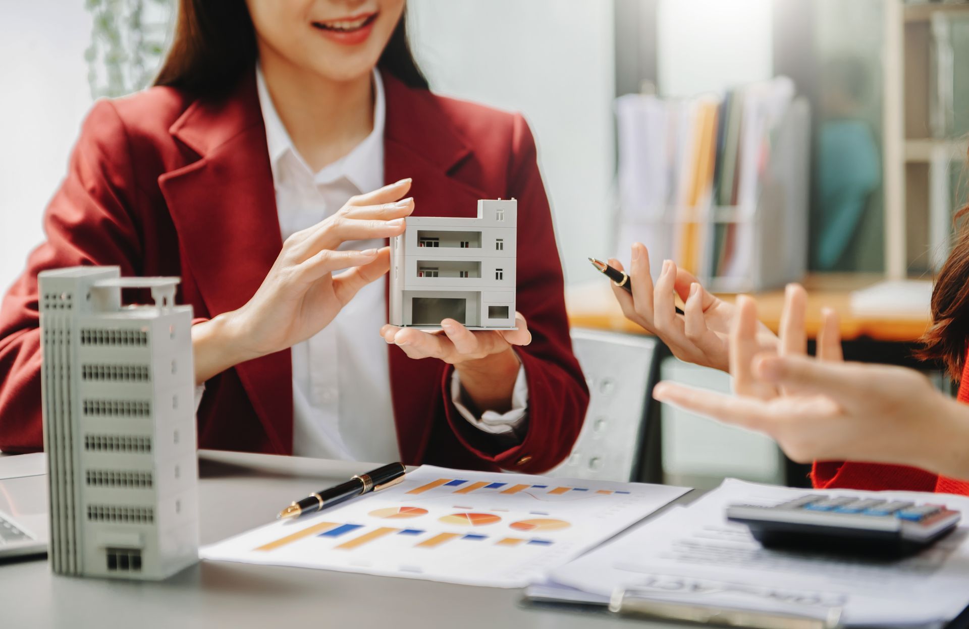 A woman is sitting at a table holding a model of a building.