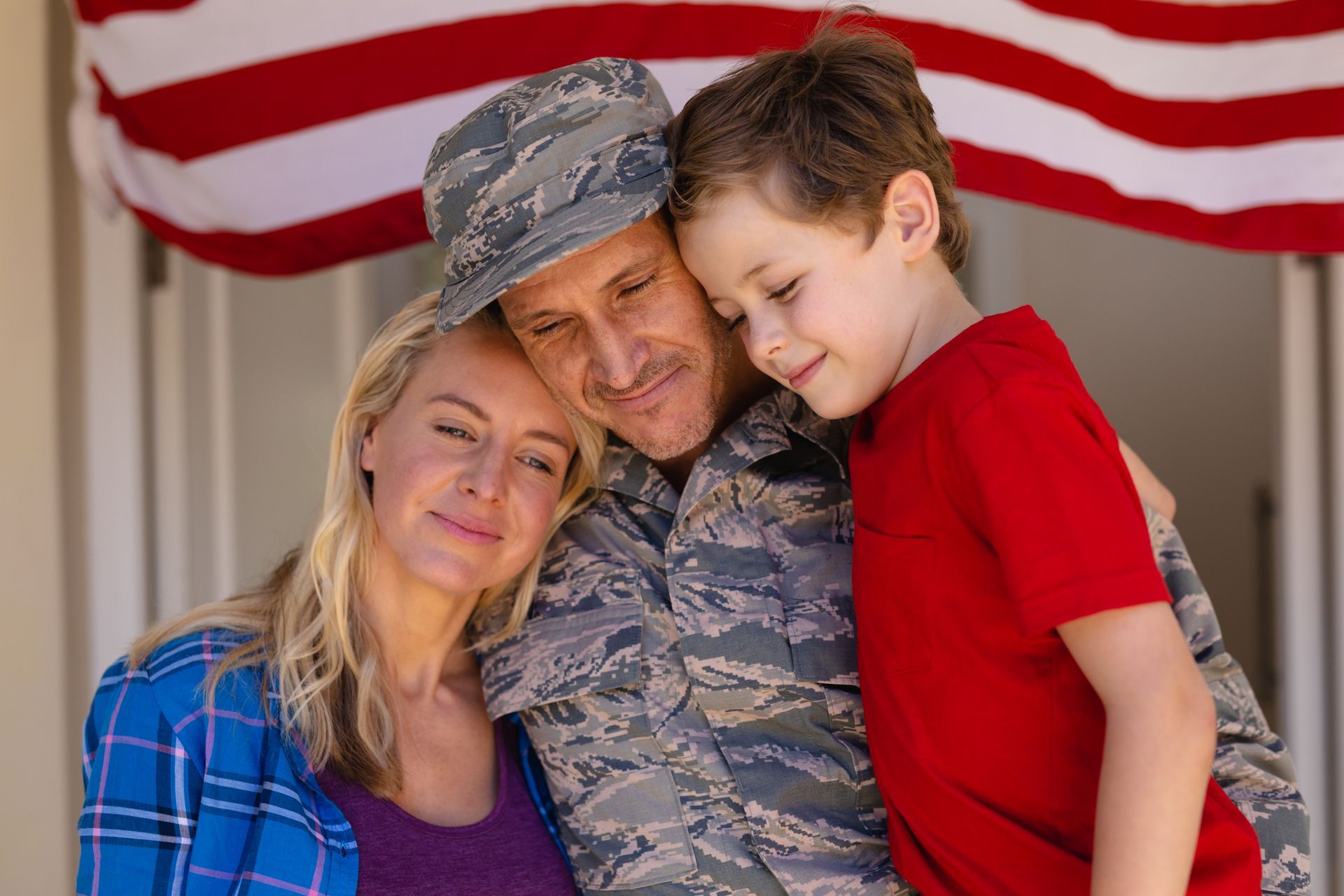 A man in a military uniform is standing next to a woman and a child in front of an american flag.