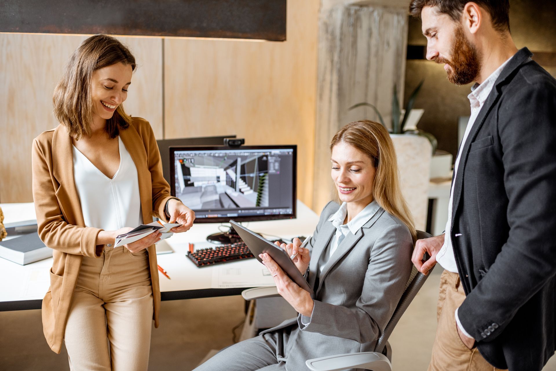 A group of people are standing around a woman sitting in a chair looking at a tablet.