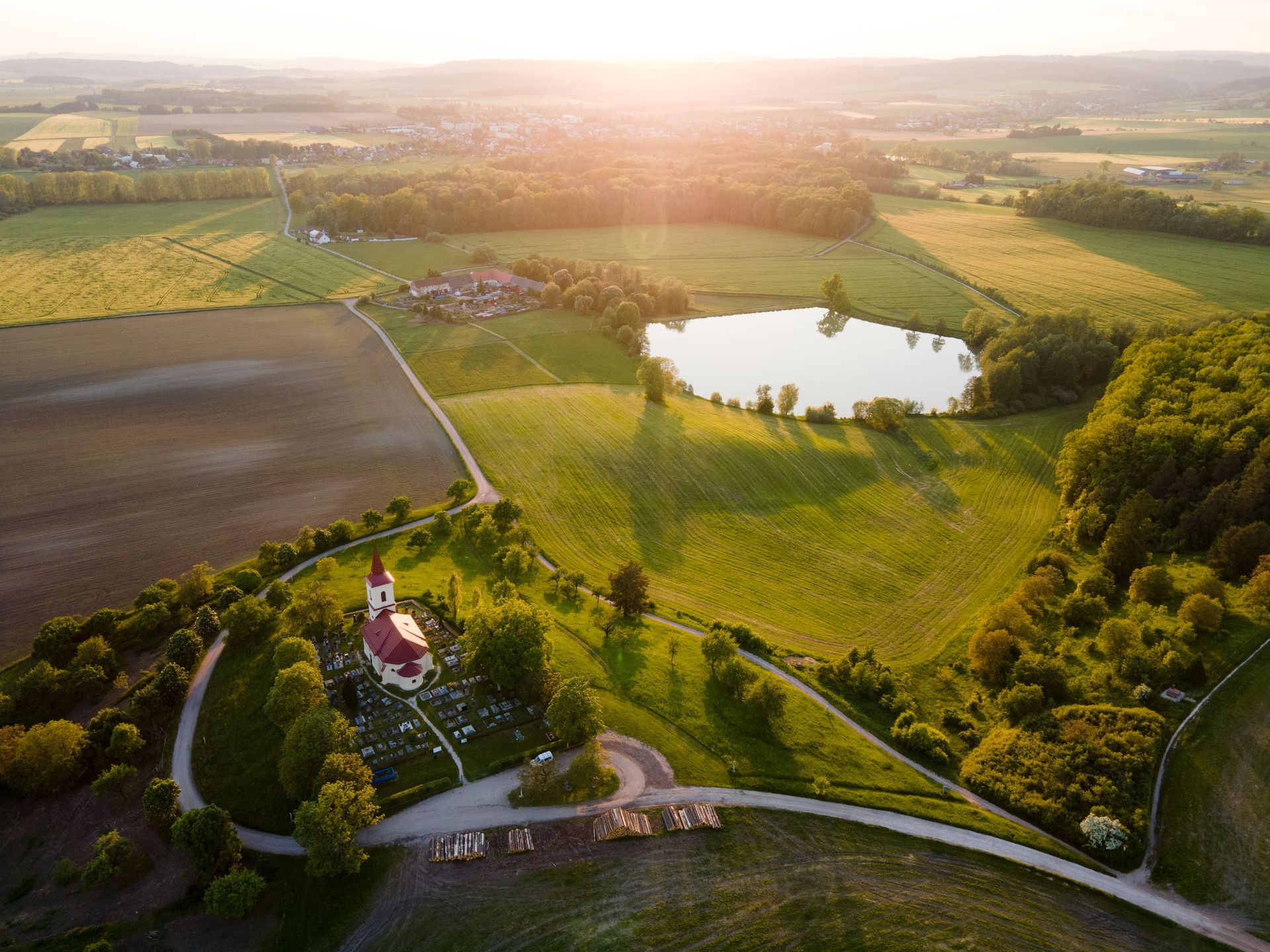 An aerial view of a church surrounded by fields and a lake.