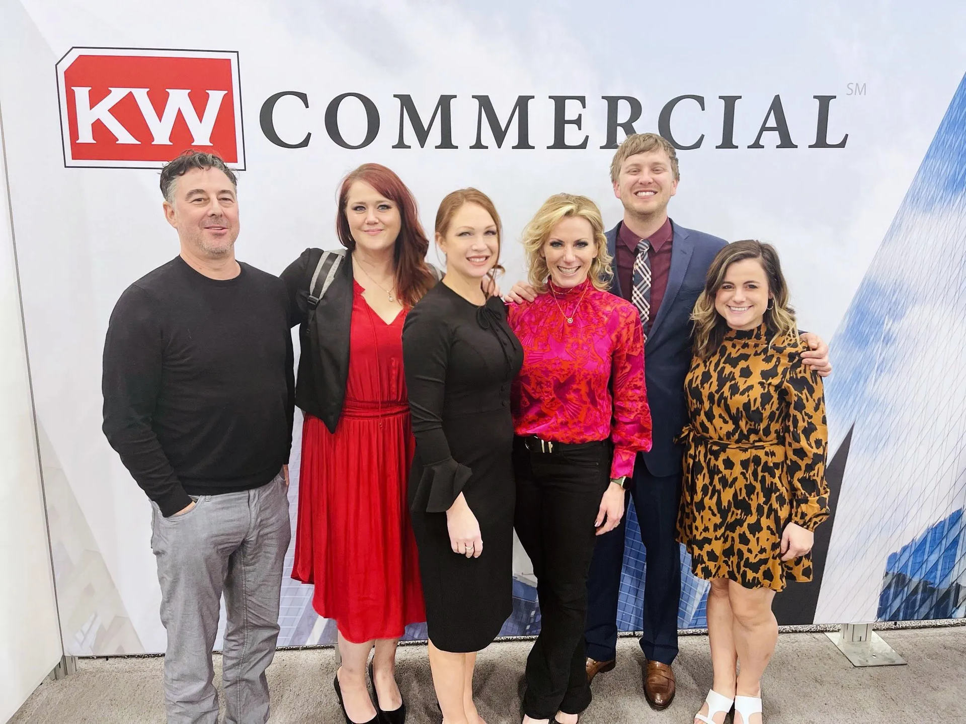 A group of people are posing for a picture in front of a kw commercial sign.