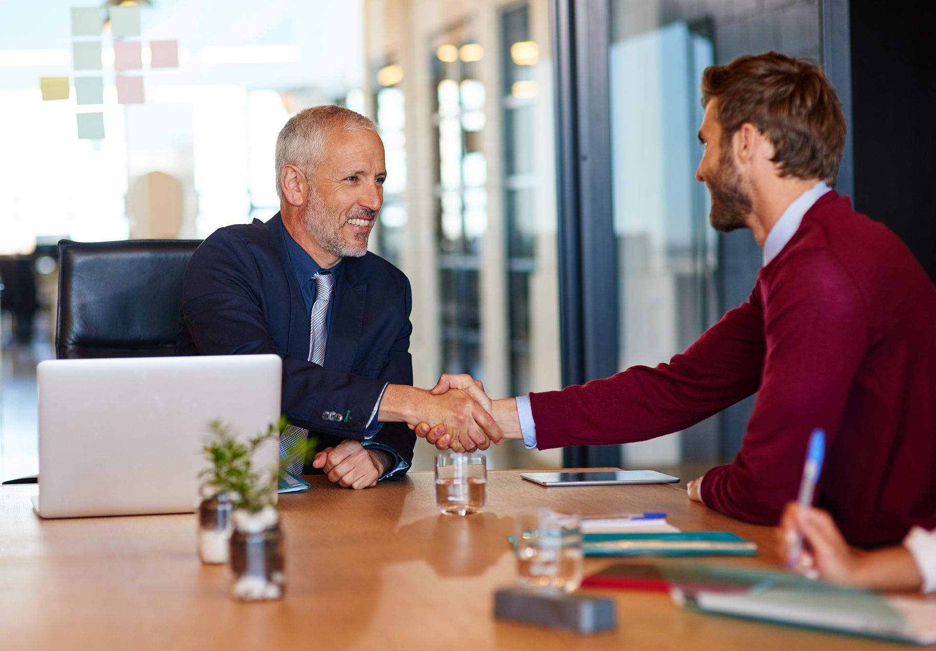 Two men are shaking hands while sitting at a table.