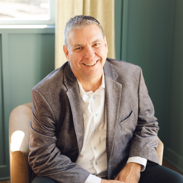 A man in a suit is sitting in a chair and smiling