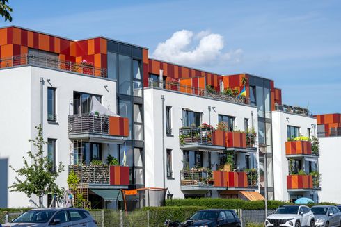 A row of apartment buildings with cars parked in front of them.