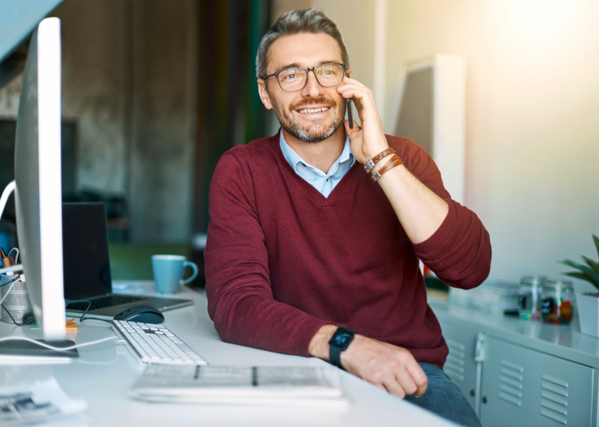 A man is sitting at a desk talking on a cell phone.