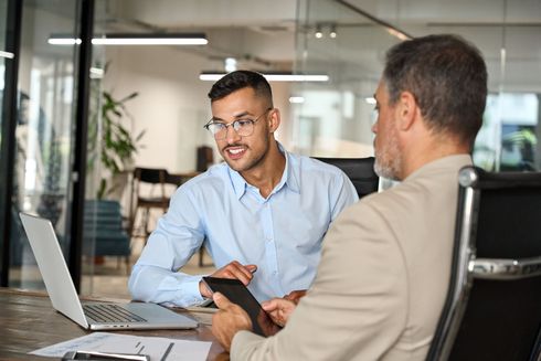 Two men are sitting at a table with a laptop and a tablet.