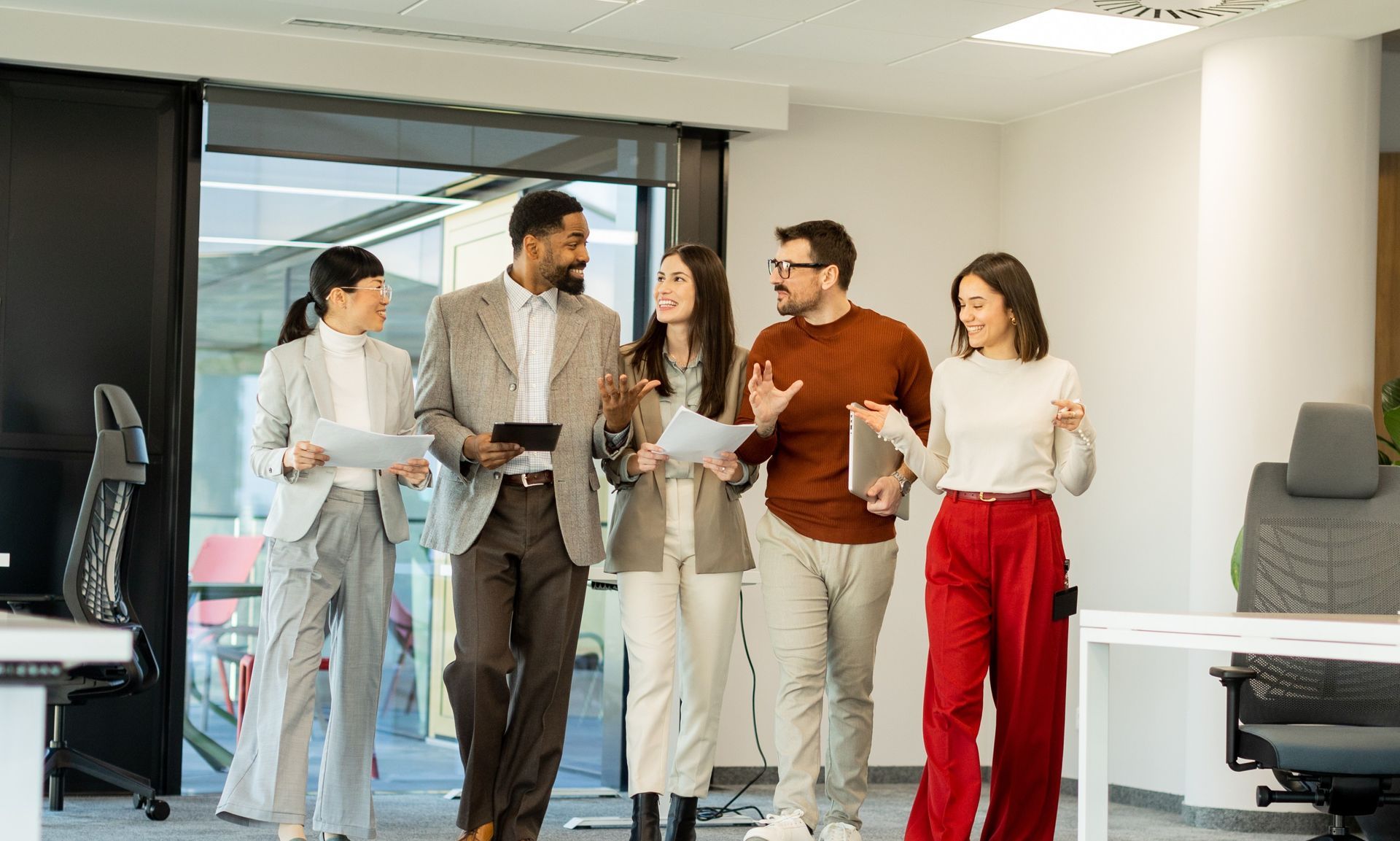 A group of people are standing in an office talking to each other.