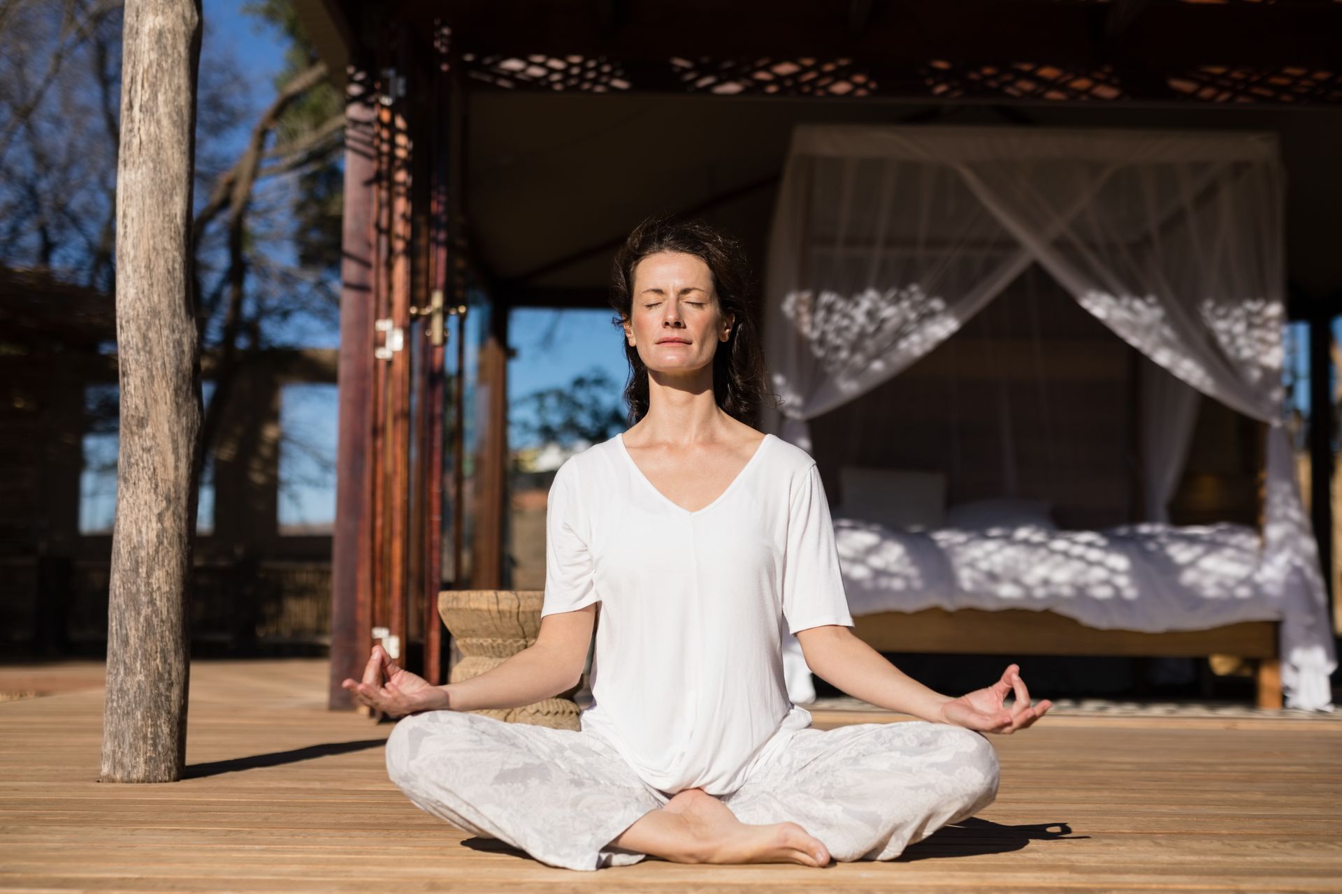 A woman is sitting in a lotus position on a wooden deck.